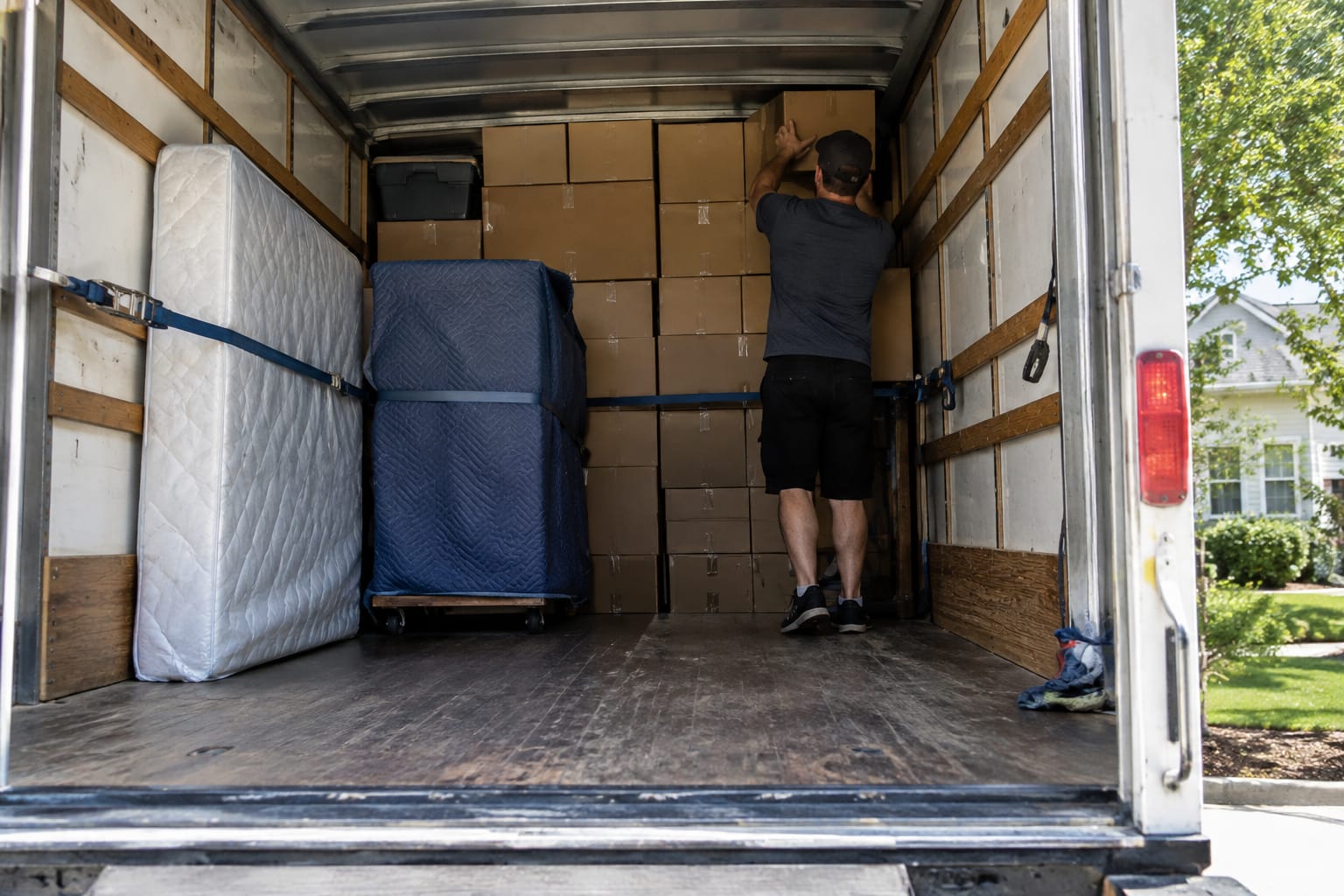 Half-loaded box truck interior with a floor-to-ceiling box wall, upright mattress, and ratchet straps across the load.
