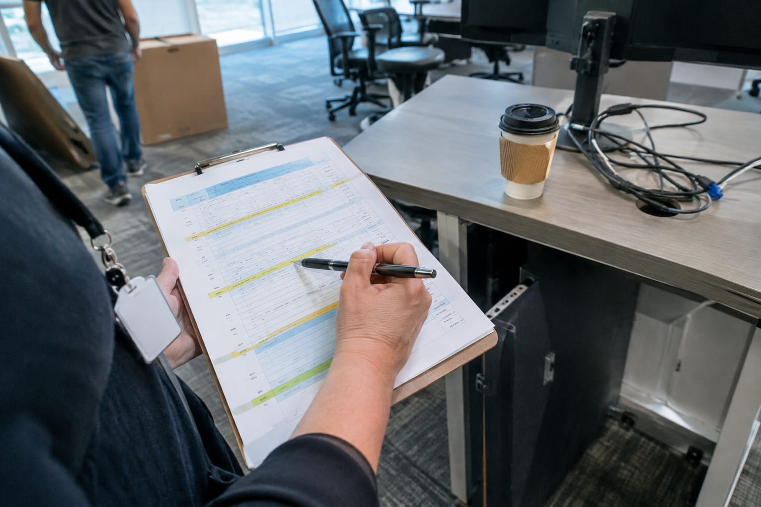 Hands holding a clipboard with a highlighted move schedule beside a badge, coffee cup, and stripped desk.