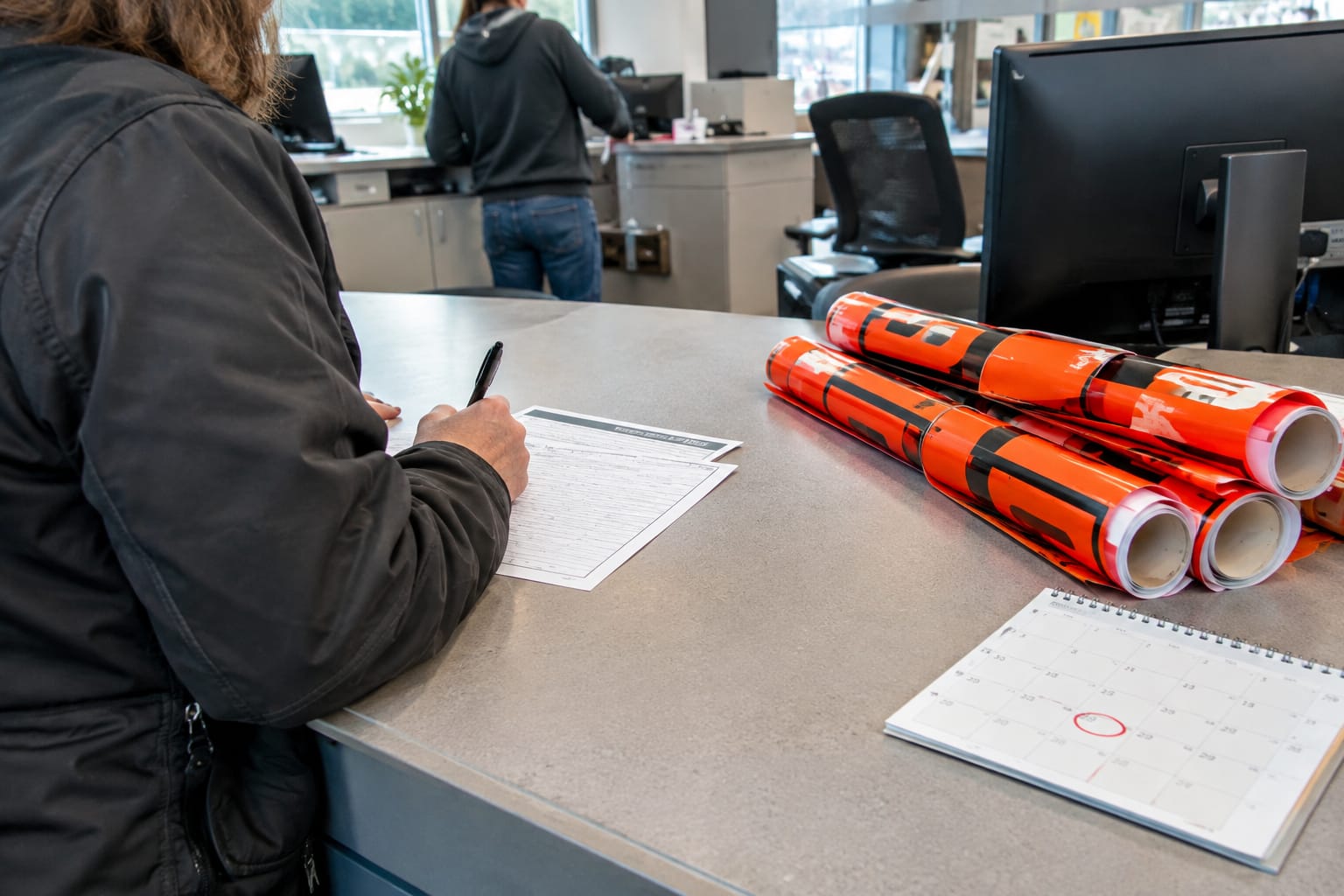Resident filling out a street-occupancy permit form beside rolled orange no-parking signs at a city counter