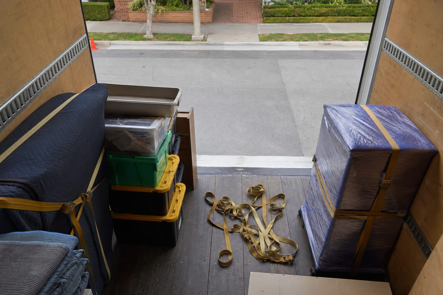 Young couple shaking hands with a mover at their doorway as crew wheels a dolly of boxes