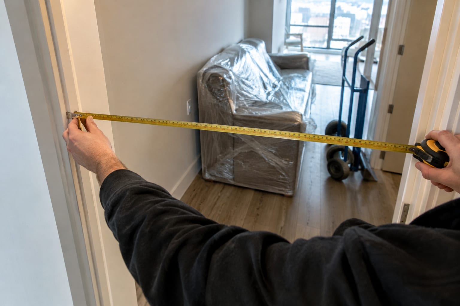 Mover measuring a narrow apartment doorway with a tape measure next to a disassembled bed frame in the hall