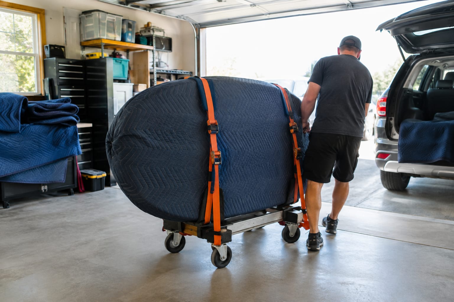 Power rack upright and weight plates secured with ratchet straps on a furniture dolly over a moving pad in a garage