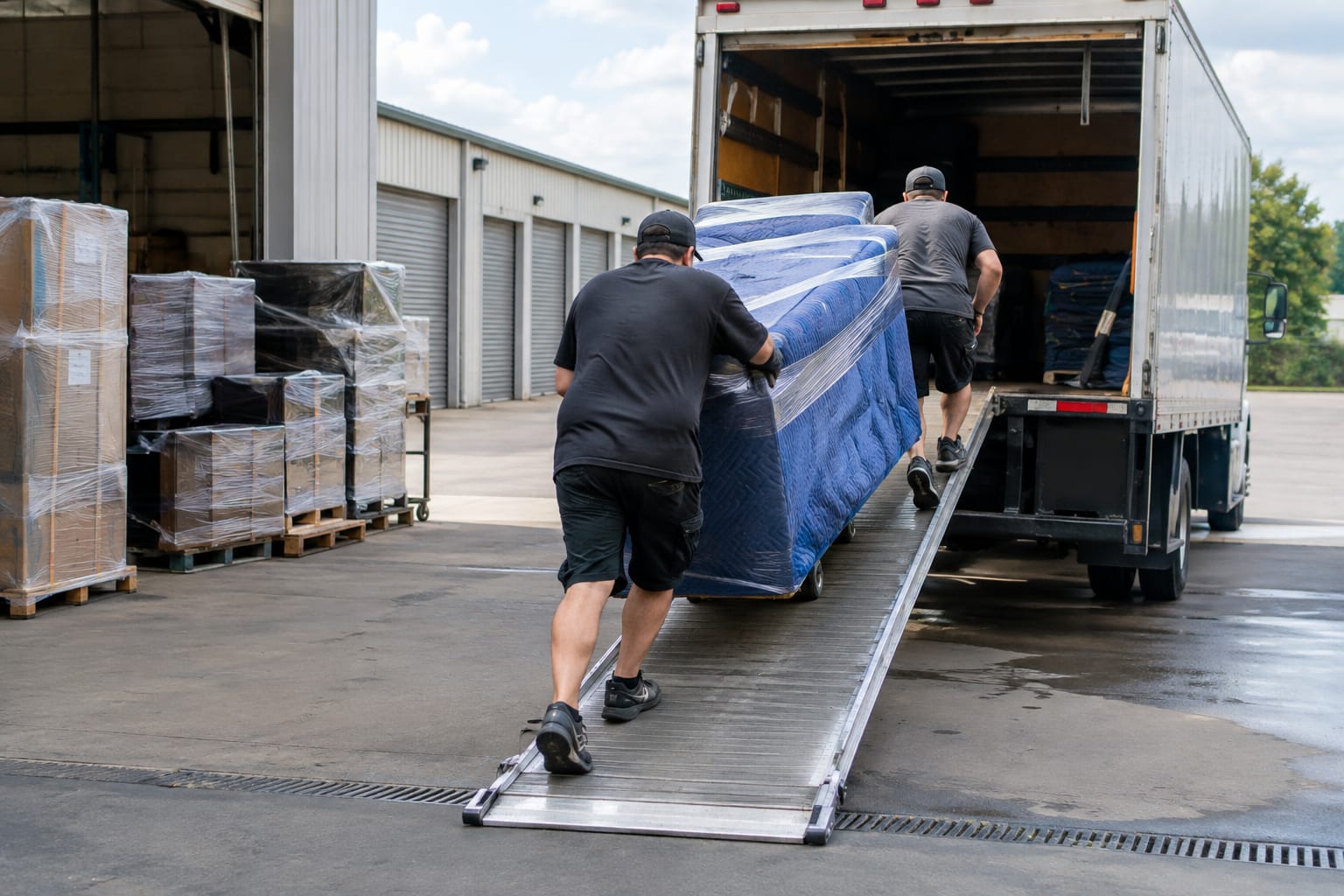 Storage facility aisle with blanket-wrapped furniture, each piece tagged with a numbered inventory sticker